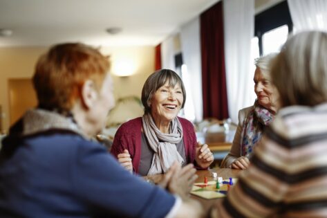 Senior adults in a senior home cheerfully playing a board game around a table.