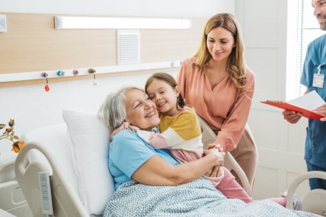 Woman with daughter visiting her mother at hospital, she is talking with doctor and showing love and care for her mother.