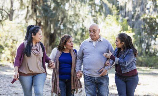 A senior Hispanic couple walking with their two adult daughters at the park on a sunny autumn day. They are side by side, holding hands, conversing.