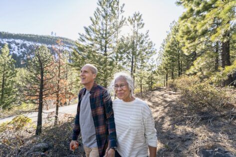 Wide angle shot featuring a Pacific Islander woman and her Caucasian husband enjoying nature on a sunny day. They are holding hands and smiling.