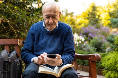 Senior man looks at his phone on a park bench.